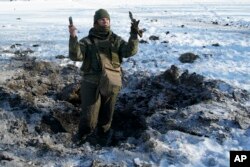 FILE - A Ukrainian soldier shows pieces of shrapnel in a crater left by an explosion in Avdiivka, Ukraine, Jan. 31, 2017.