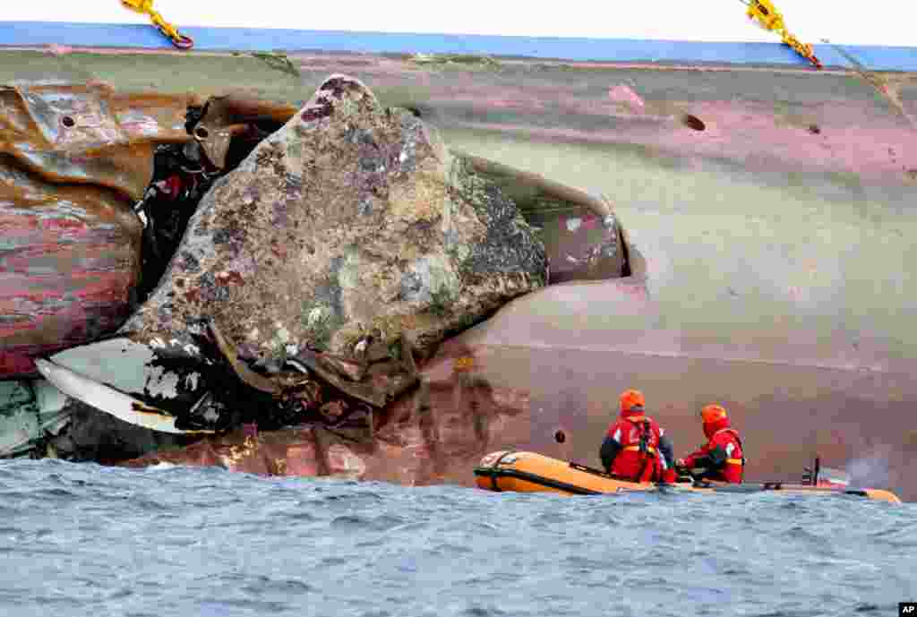 Firefighters on a dinghy look at a rock emerging from the side of the ship on Sunday. (AP)