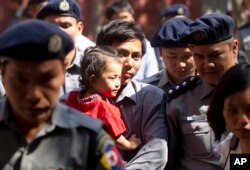 Reuters journalist Kyaw Soe Oo carries his daughter as he is escorted by Myanmar police to trial after a break, Feb. 1, 2018, outside of Yangon, Myanmar. A lawyer for the two Reuters journalists Wa Lone and Kyaw Soe Oo, charged with illegally handling gov