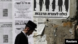 An ultra-Orthodox Jewish man walks past a street poster in Jerusalem's Mea Shearim neighborhood, inviting the public to a protest against government plans to draw more ultra-Orthodox men into the conscript army, June 3, 2013. 