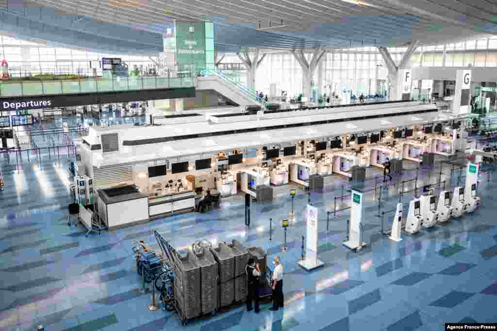 Staff members stand by in a mostly empty departures hall at Tokyo&#39;s Haneda international airport.&nbsp;More than 370,000 people are in left in limbo by Japan&#39;s coronavirus border rules, which bar almost all new arrivals. Airport workers stand by at a mostly empty departures area of Haneda International near Tokyo. Japan&#39;s coronavirus border rules bar almost all new arrivals to the country.&nbsp;