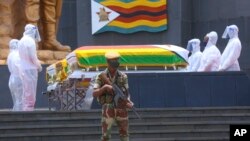 Pallbearers stand next to the coffins of three top government officials prior to their burial, at the National Heroes Acre in Harare, Wednesday, Jan. 27, 2021. 