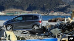 A car passes in front of tsunami debris piled up on the wharf in Ofunato, Iwate Prefecture nearly one year after the March 11 tsunami devastated the area, January 15, 2012.