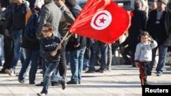 A Tunisian boy waves a flag as he runs during a rally to mark the third anniversary of the Tunisian revolution, in Tunis, Tunisia, Dec. 17, 2013.