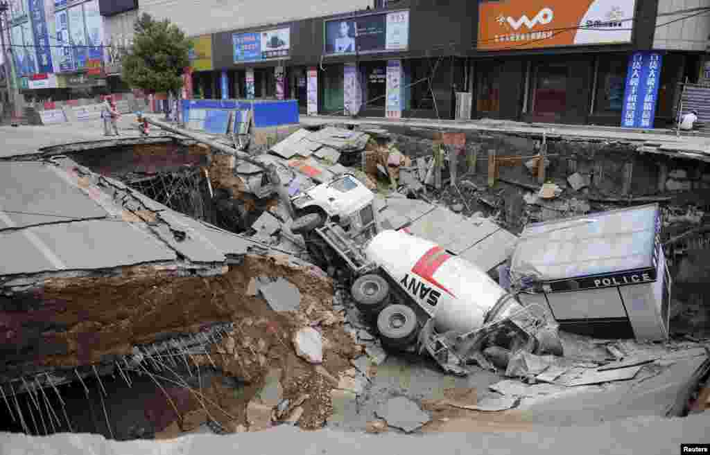 Workers stand next to a pit after a truck and a police kiosk fell into a cave-in on a street in Dingyuan county, Anhui province, China.