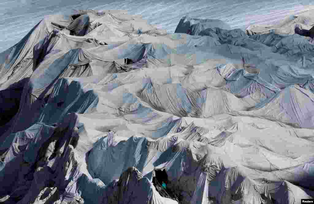 ស្ត្រី​ម្នាក់​ឈប់​ដើម្បីថត​នៅ​ខាង​ក្រៅ​រូង​នៅ​ Rhone Glacier នៅ​ភ្នំ&nbsp;Furka ប្រទេស​ស្វ៊ីស។