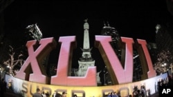 In this photo taken with a fisheye lens, football fans pose for photos in front of the Super Bowl XLVI logo on Monument Circle in Indianapolis, February 1, 2012.