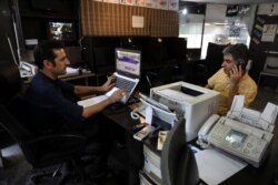 FILE - An internet cafe manager works on his computer as a man talks on his cell phone, in Tehran, Iran, July 25, 2019.