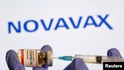 FILE PHOTO: A woman holds a small bottle labeled with a "Coronavirus COVID-19 Vaccine" sticker and a medical syringe in front of displayed Novavax logo in this illustration