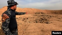 A member of Iraqi security forces gestures towards a mass grave for corpses in the town of Hammam al-Alil which was seized from Islamic State last week, Nov. 9, 2016. 