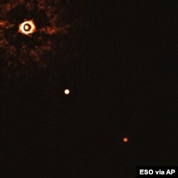 This image from the European Southern Observatory, July 2020, shows the star TYC 8998-760-1, upper left, and two exoplanets. The image was captured by blocking the light from the star, allowing for the fainter planets to be detected.