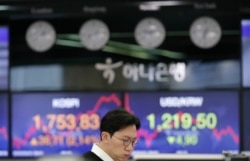 A currency trader watches computer monitors near screens showing the Korea Composite Stock Price Index (KOSPI), left, and the foreign exchange rate between U.S. dollar and S. Korean won at the foreign exchange dealing room in Seoul, March 31, 2020.