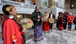 Earth Feather Sovereign, left, of the Confederated Tribes of the Colville Reservation, playing drums and signing in the Capitol Rotunda after Washington Gov. Jay Inslee signed a bill into law, Wednesday, April 24, 2019, in Olympia, Wash.
