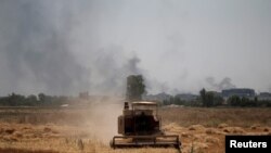 FILE - Smoke billows from the positions of the Islamic State militants as a harvester gathers the wheat crop from a field in western Mosul, Iraq, June 19, 2017.