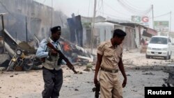 FILE - Somali police walk around the scene of an explosion near the entrance of the airport in Mogadishu, Feb. 13, 2014.