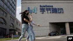 FILE - In this Aug. 7, 2020, file photo, women wearing masks to prevent the spread of the coronavirus chat as they pass by the headquarters of ByteDance, owners of TikTok, in Beijing, China.