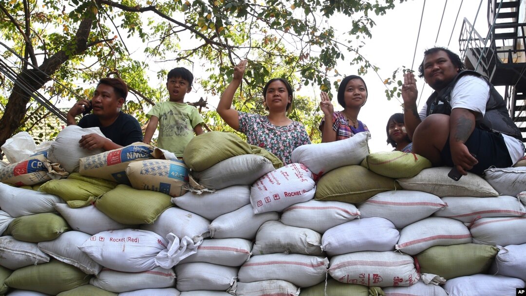 People flash the three-fingered symbol of resistance from behind a barricade of sacks blocking a road in Mandalay, Myanmar, March 5, 2021.