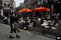 People sit on a street closed to traffic to try to reduce the spread of coronavirus so bars, cafes and restaurants can continue to stay open, in London, Sept. 19, 2020. New lockdown restrictions in England appear to be in the cards.