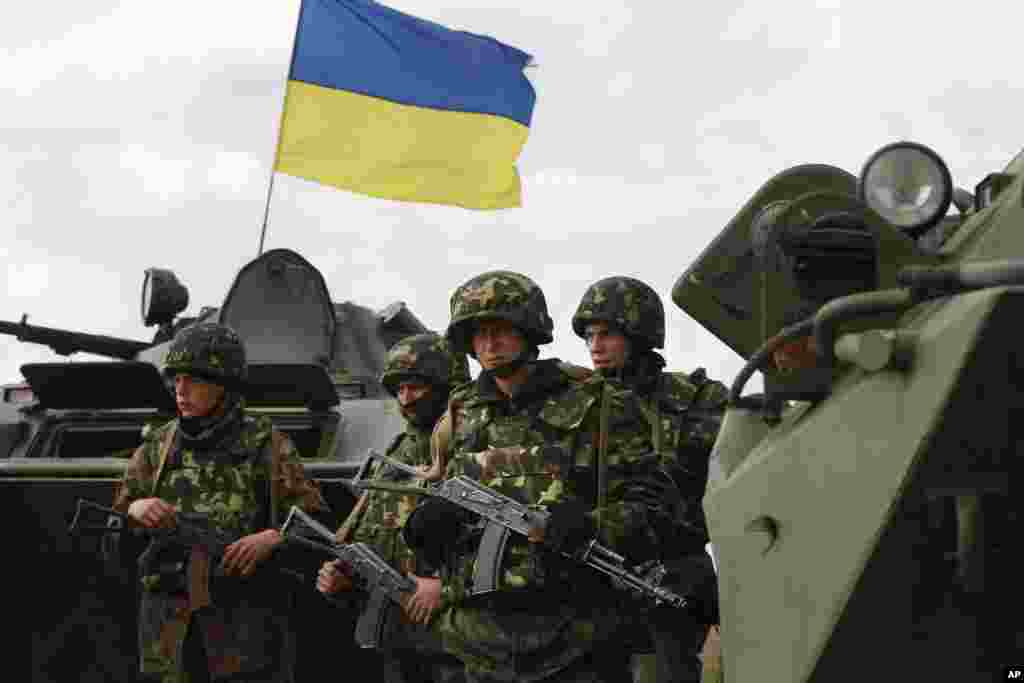 Ukrainian soldiers stand near APCs, that fly a Ukrainian flag, as army troops receive ammunition in a field on the outskirts of Izyum, April 15, 2014.