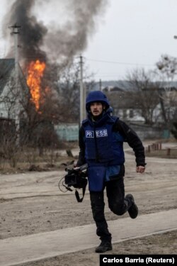 Seorang jurnalis berlari mencari perlindungan setelah penembakan di satu-satunya rute pelarian yang digunakan penduduk setempat, saat pasukan Rusia maju menuju ibu kota, di Irpin, dekat Kyiv, Ukraina 6 Maret 2022. (Foto: REUTERS/Carlos Barria)