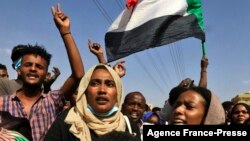 Sudanese protesters flash victory signs and lift natioanl flags as they demonstrate in Khartoum to denounce overnight detentions by the army of government members, on Oct. 25, 2021.