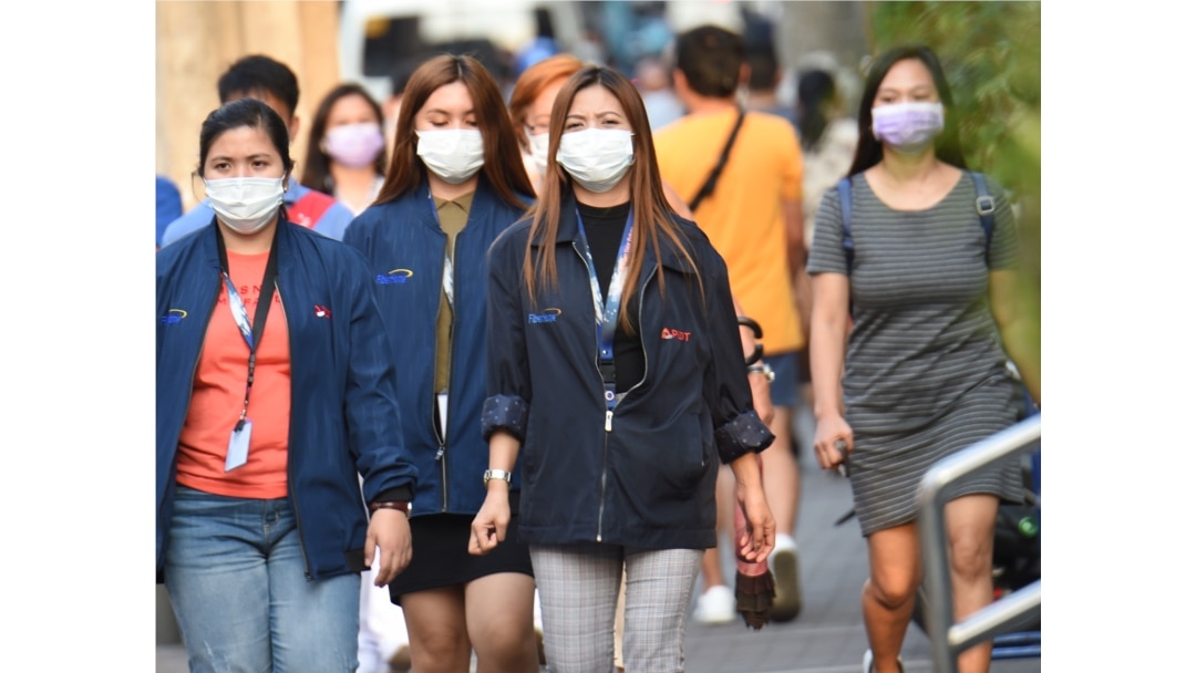 Office employees wearing facemasks walk along a street in Manila on January 30, 2020. -