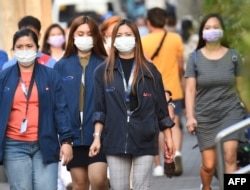 Office employees wearing facemasks walk along a street in Manila on January 30, 2020. -