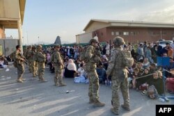 U.S. soldiers stand guard as Afghan people wait to board a U.S. military aircraft to leave Afghanistan, at the military airport in Kabul, August 19, 2021.