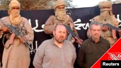 FILE - French nationals Philippe Verdon and Serge Lazarevic are seen surrounded by masked men holding guns in an undisclosed location in Mali, in this undated handout picture. 