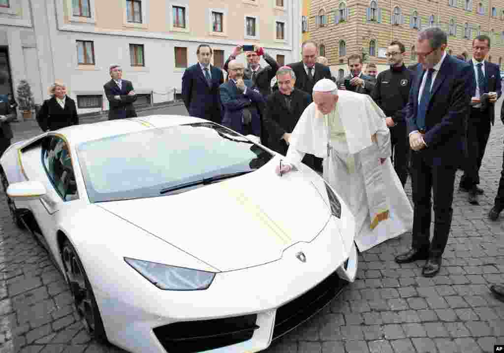 Pope Francis writes on a Lamborghini car donated to him by the luxury sports car maker, at the Vatican. The car will be auctioned off by Sotheby&#39;s, with the money going to charities including one aimed at helping rebuild Christian communities in Iraq that were devastated by the Islamic State group.