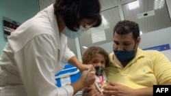 FILE - Pedro Montano holds his daughter Roxana Montano, 3, while she is vaccinated against COVID-19 with a Cuban vaccine, at Juan Manuel Marquez hospital in Havana, August 24, 2021.