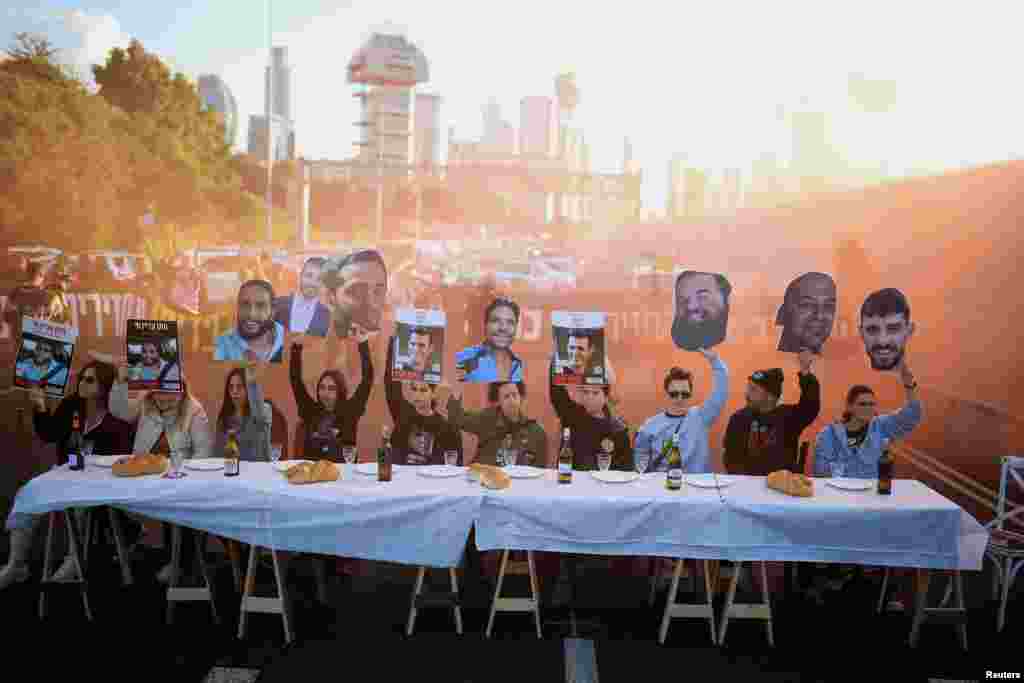 People sitting at a table representing the Friday dinner table in the Jewish tradition hold up images of hostages kidnapped during the deadly Oct. 7, 2023 attack, as supporters block a road to demand the release of their loved ones in Tel Aviv, Israel.