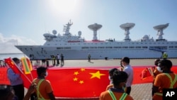 FILE - Sri Lankan port workers hold a Chinese national flag to welcome Chinese research ship Yuan Wang 5, bristling with surveillance equipment, as it arrives in Hambantota International Port in Hambantota, Sri Lanka, on Aug. 16, 2022.