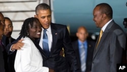Kenya Devlet Başkanı Uhuru Kenyatta (sağda) dönemin ABD Başkanı Barack Obama'nın 24 Temmuz 2015 tarihinde Kenya'nın başkenti Nairobi'deki Kenyatta Uluslararası Havalimanı'na varışının ardından üvey kız kardeşi Auma Obama'ya sarılışını izliyor.
