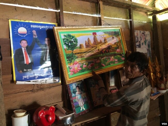 លោក ចេក ឈុន អាយុ៦៧ឆ្នាំ បង្ហាញរូបថតរបស់មេដឹកនាំគណបក្សសង្រ្គោះជាតិ ដែលត្រូវបានព្យួរនៅក្នុងផ្ទះកូនប្រុសរបស់លោក។ (ស៊ុន ណារិន/VOA)
