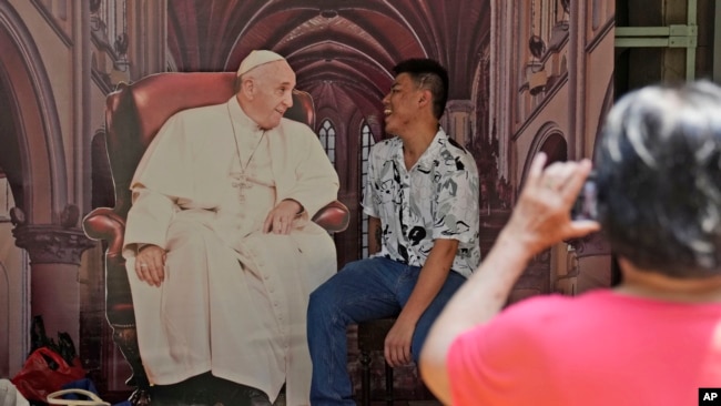 Seorang pria berfoto dengan gambar Paus Fransiskus yang dipasang di Gereja Katedral Jakarta menjelang kunjungan Paus ke Jakarta, pada 1 September 2024. (Foto: AP/Dita Alangkara)