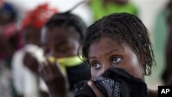 海地妇女用手绢蒙住鼻子和嘴，在医院里等待自己的孩子得到治疗