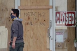 A man wears a face mask while walking past a handwritten sign advising that nothing of value is inside a boarded up Union Nails salon during the coronavirus outbreak in San Francisco, May 12, 2020.