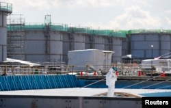 FILE - A worker, wearing protective suits and masks, takes notes in front of storage tanks for radioactive water at Tokyo Electric Power Co's (TEPCO) tsunami-crippled Fukushima Daiichi nuclear power plant in Okuma town, Fukushima prefecture, Japan, Feb.10, 2016.