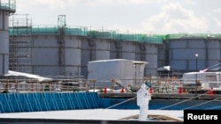 FILE - A worker, wearing protective suits and masks, takes notes in front of storage tanks for radioactive water at Tokyo Electric Power Co's (TEPCO) tsunami-crippled Fukushima Daiichi nuclear power plant in Okuma town, Fukushima prefecture, Japan, Feb.10, 2016.