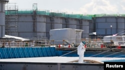 A worker, wearing protective suits and masks, takes notes in front of storage tanks for radioactive water at Tokyo Electric Power Co's (TEPCO) tsunami-crippled Fukushima Daiichi nuclear power plant in Okuma town, Fukushima prefecture, Japan, Feb.10, 2016.