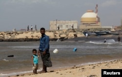 FILE - A man stands with his son on the beach near the Kudankulam nuclear power project in the southern Indian state of Tamil Nadu.
