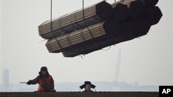 Port workers watch as steel pipes are unloaded from freighter at Cao Feidian Port, Tangshan, Hebei province, China, Feb. 20, 2012.