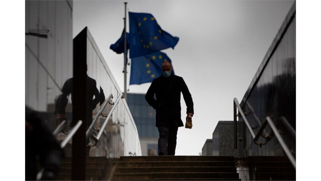 A man walks past EU flags flapping in the wind in front of the European Union headquarters in Brussels, Dec. 21, 2020.