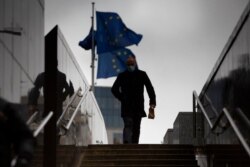 A man walks past EU flags flapping in the wind in front of the European Union headquarters in Brussels, Dec. 21, 2020.
