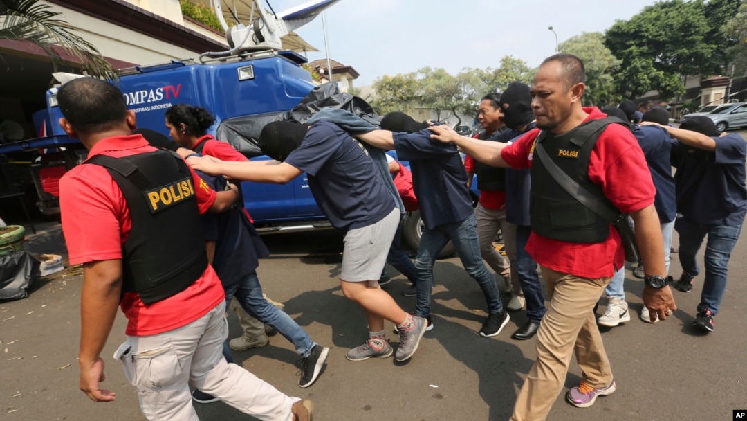 FILE - Police officers escort men arrested in a raid on a gay sauna at North Jakarta police headquarters in Jakarta, Indonesia, May 22, 2017. Authorities in Indonesia's West Java province announced the creation of a task force charged with investigating activities by gays.