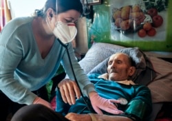 Dr. Viktoria Mahnych, wearing face mask against coronavirus, checks on a COVID-19 patient with a stethoscope at at his home in Iltsi village, Ivano-Frankivsk region of Western Ukraine, Wednesday, Jan. 6, 2021. (AP Evgeniy Maloletka)