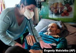 Dr. Viktoria Mahnych, wearing face mask against coronavirus, checks on a COVID-19 patient with a stethoscope at at his home in Iltsi village, Ivano-Frankivsk region of Western Ukraine, Wednesday, Jan. 6, 2021. (AP Evgeniy Maloletka)