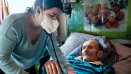 Dr. Viktoria Mahnych, wearing face mask against coronavirus, checks on a COVID-19 patient with a stethoscope at at his home in Iltsi village, Ivano-Frankivsk region of Western Ukraine, Wednesday, Jan. 6, 2021. (AP Evgeniy Maloletka)
