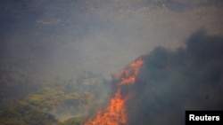 Flames rise next to a house as a wildfire burns in the village of Sinterina, Greece, Aug. 16, 2021.